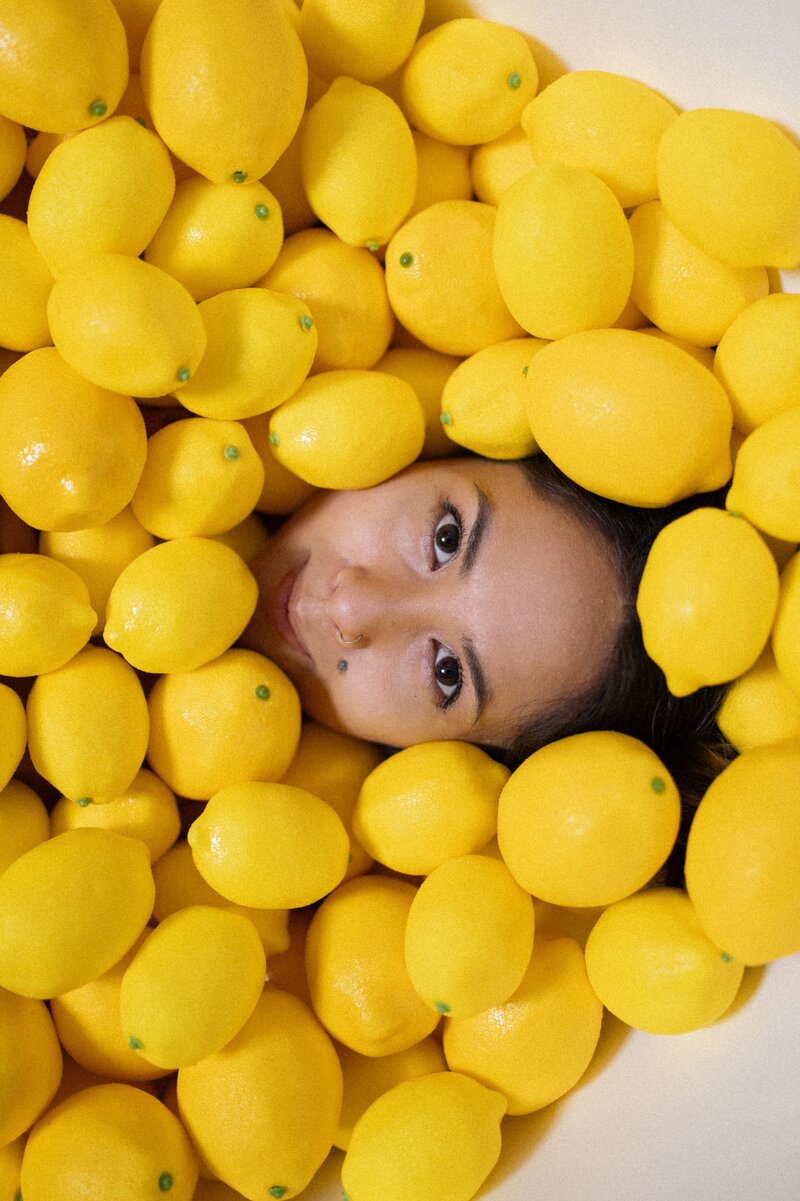Woman's face peeks out of pile of lemons.