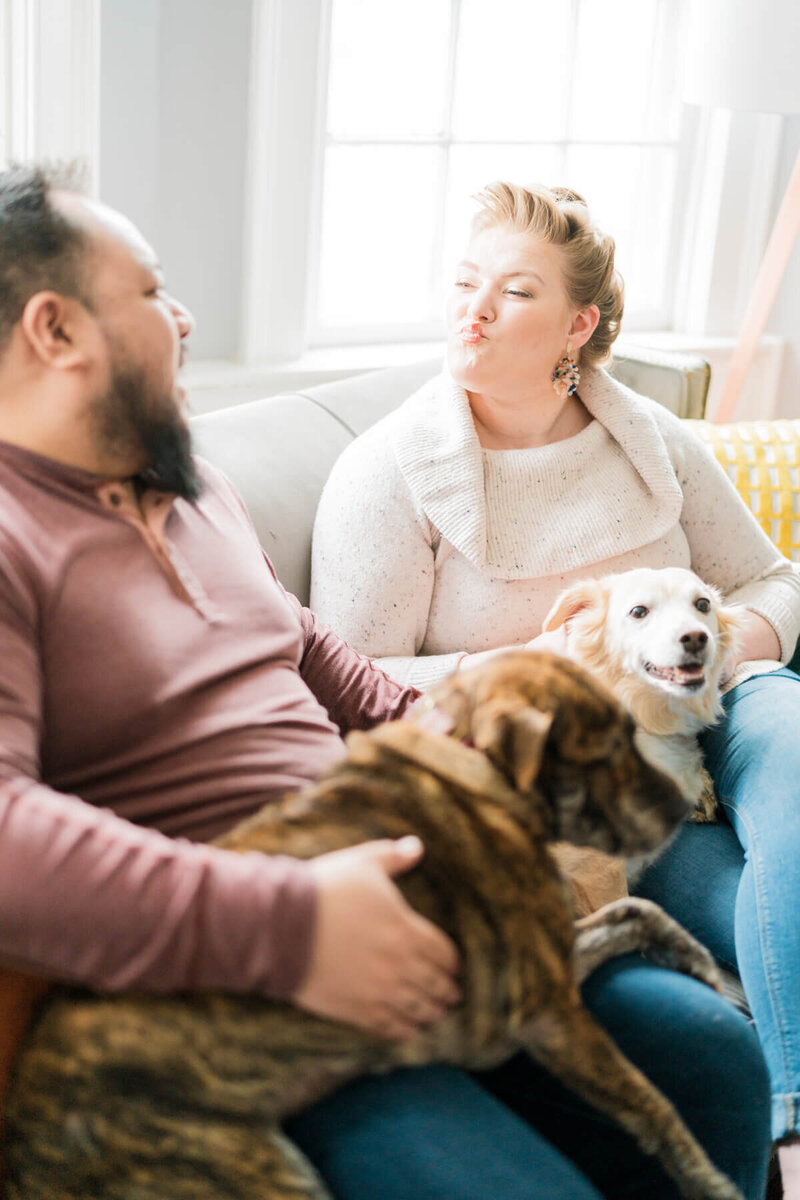 Becca Mai sitting on a couch blowing a kiss to her husband Phil Mai while their dogs Carly and Dori are on their laps