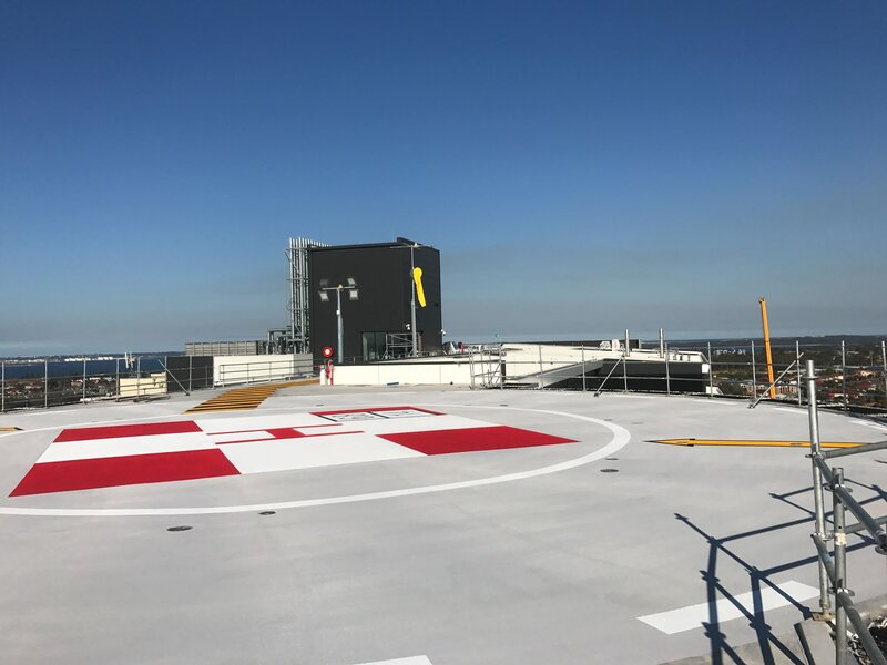 A red and white helicopter landing area line marking on the roof of a hospital building.