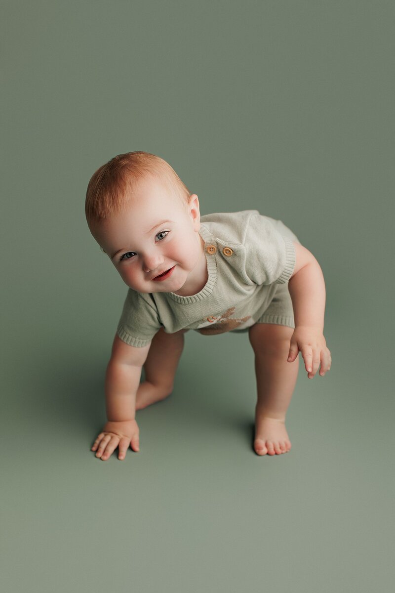 Baby crawling toward camera with huge smile during milestone photo shoot