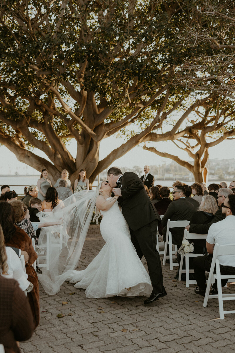 Bride and groom share a kiss at their outdoor Long Beach wedding ceremony, coordinated through full service planning by Beyond the Event and photographed by Kellie Jane Photography.