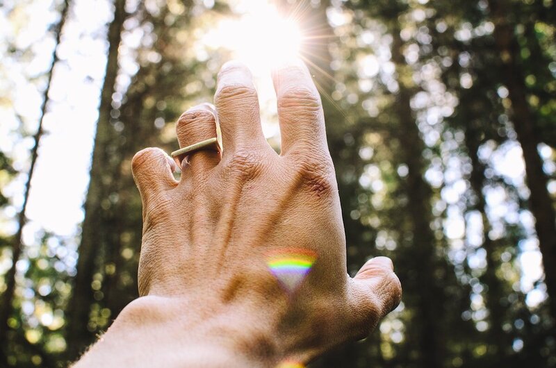 Hand reaching into the sun with a small rainbow.