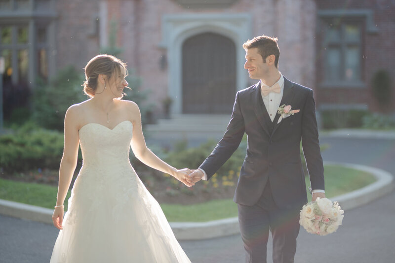 Elegant image of the bride and groom walking hand in hand in front of a stunning château along the Richelieu River — a timeless scene from a prestigious wedding in Quebec