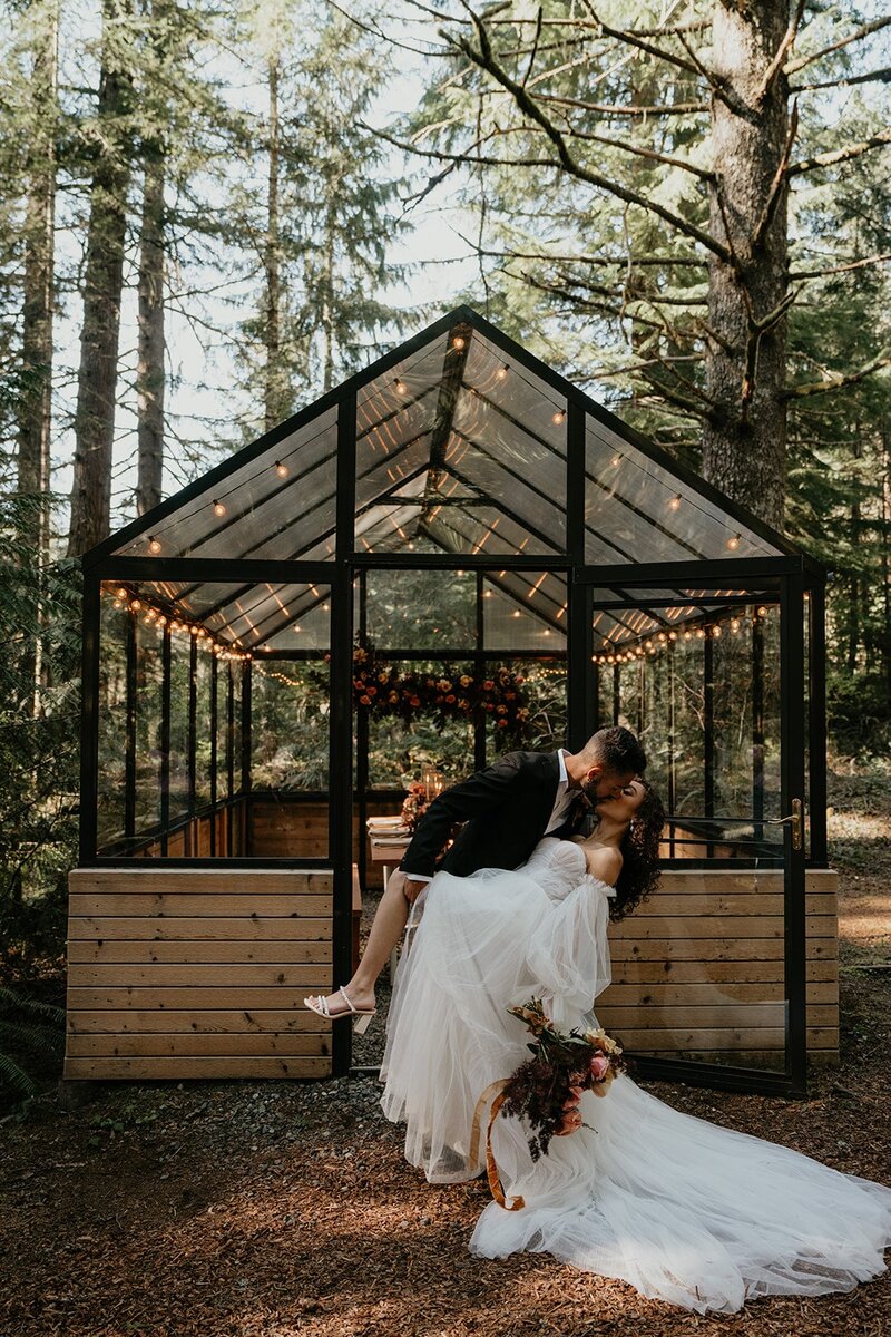 Groom dips bride back for a kiss in front of the Woodlands House wedding venue in the forest in Oregon