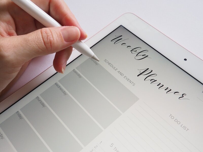 Shows a digital weekly planner on an ipad with someone holding a stylus above it