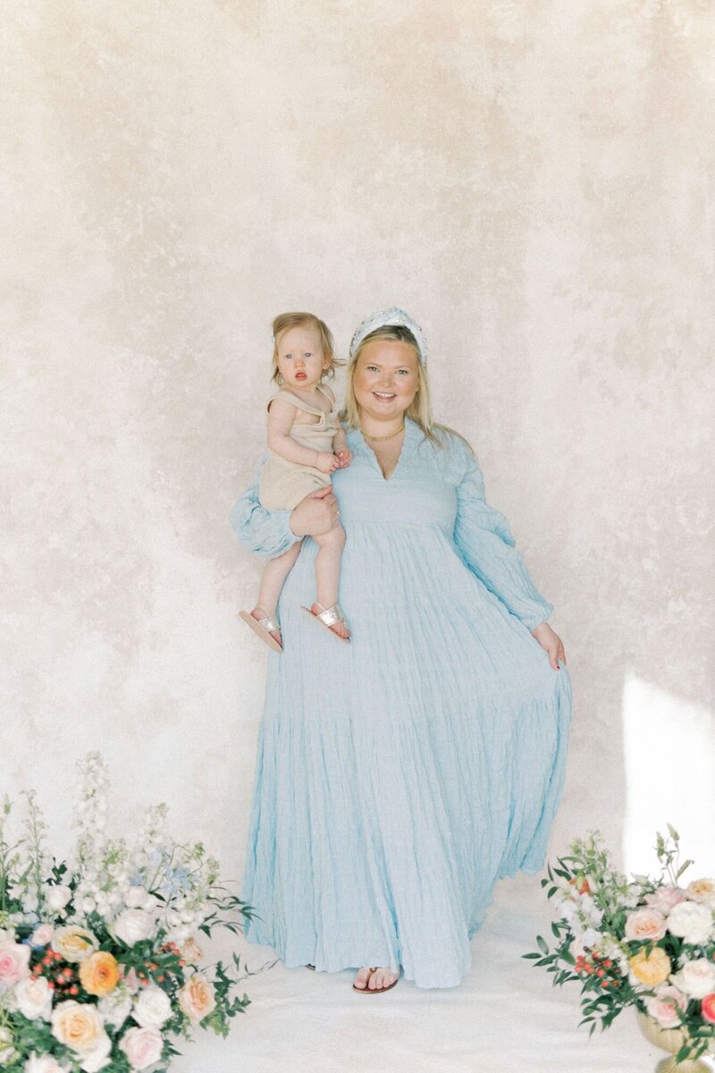 A woman holds daughter in her arms wearing a blue dress.