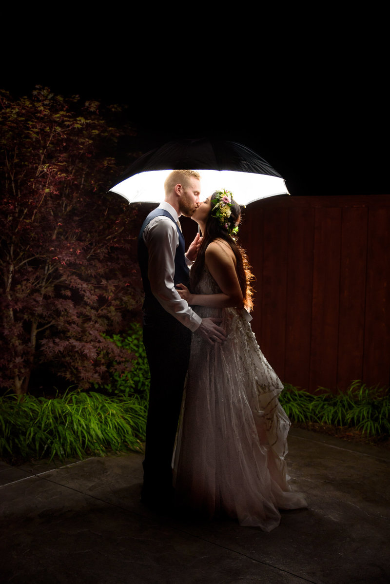 Bride and groom kiss under a lit unbrella