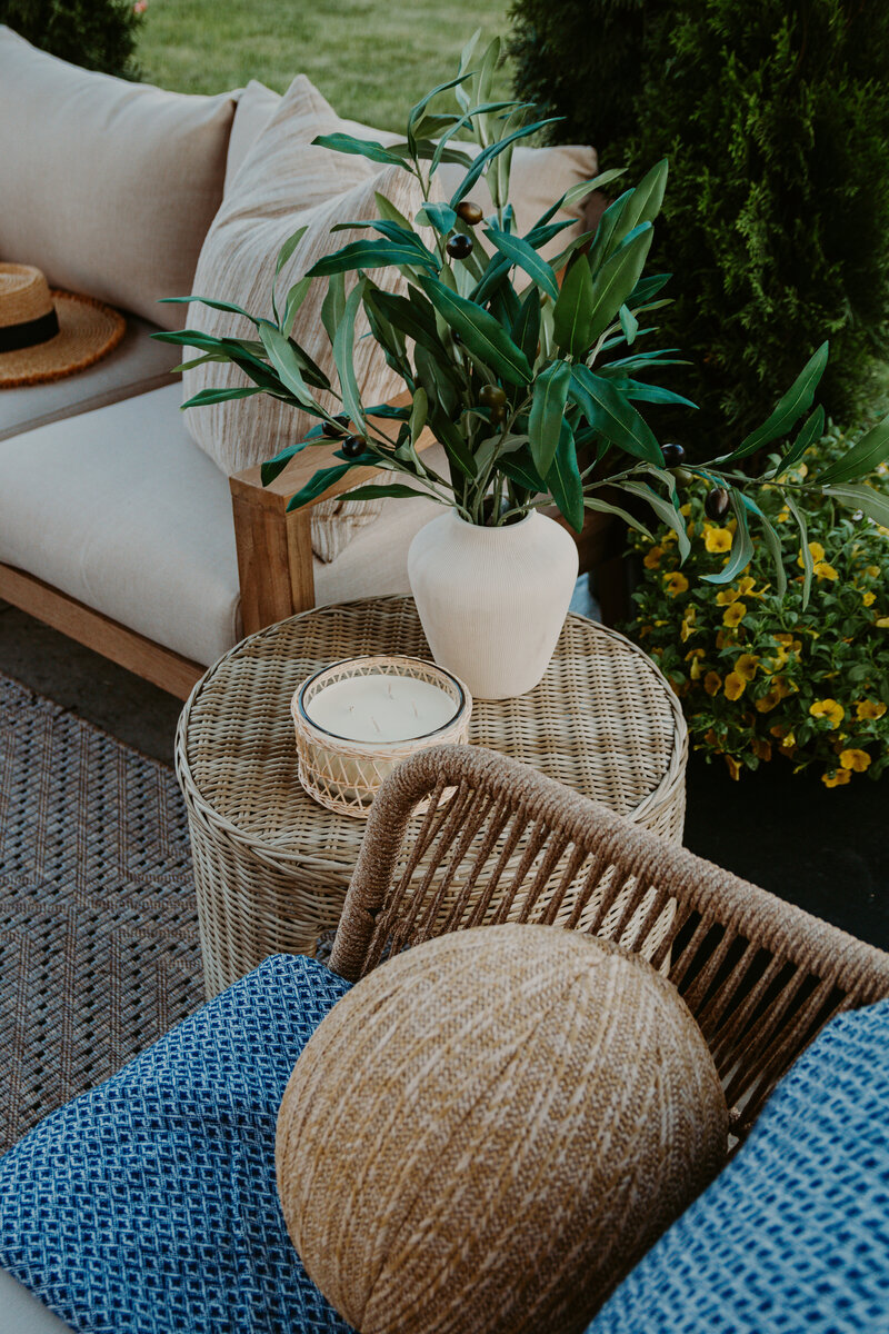 Outdoor wicker side table with candle and vase with olive branches