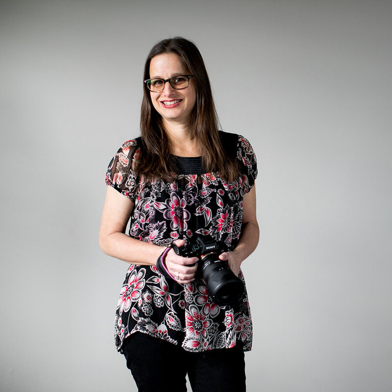 A portrait showcasing the owner of Her Story Images as she confidently holds her camera, dressed in a floral patterned shirt