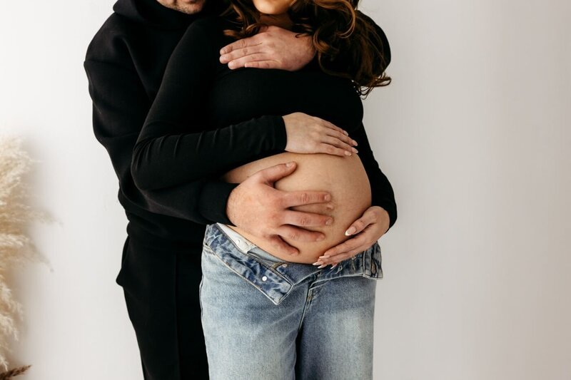 A tender moment between expecting parents, with their hands lovingly touching the pregnant belly. Maternity photography session by Ruaa Hamdan Photography in Altrincham, UK