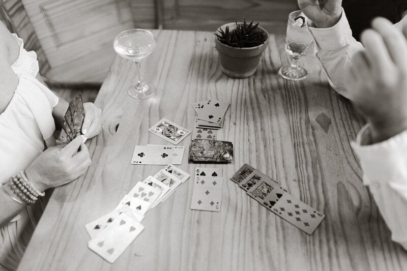 A black and white candid photo of a couple playing cards while drinking cocktails