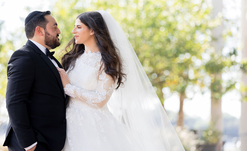 Bride holding groom with hand on chest as they look into each other's eyes.