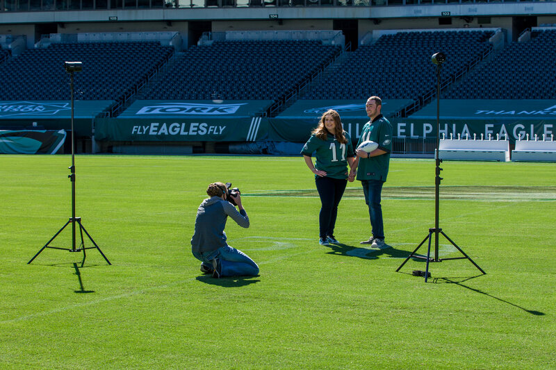 Jen Stitt capturing a special moment with an engaged couple at Lincoln Financial Field, home of the NFL Eagles, during an engagement session, blending romance with the iconic atmosphere of the stadium.