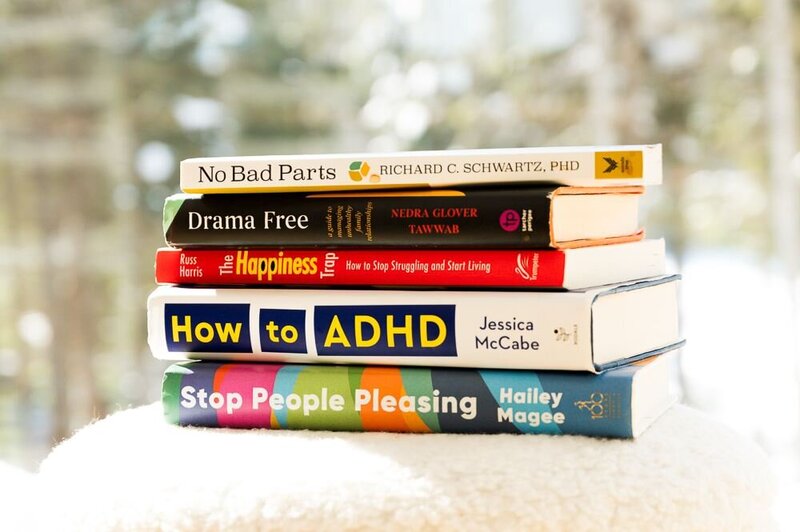 A stack of therapist-recommended books resting on a white chair, showcasing a cozy reading space.