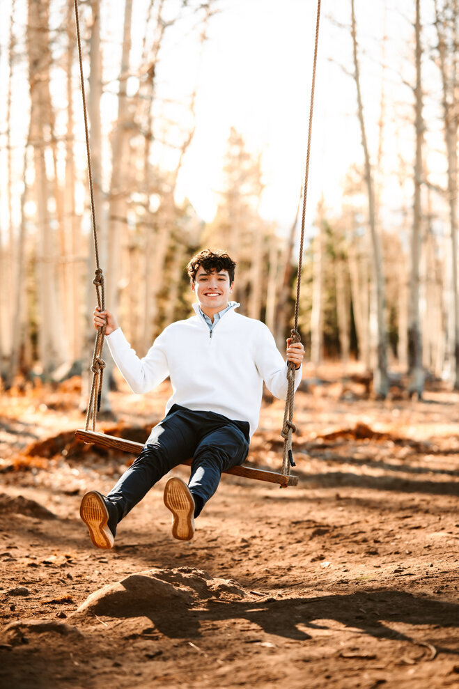 Senior graduate swinging on a swing in the aspen trees.