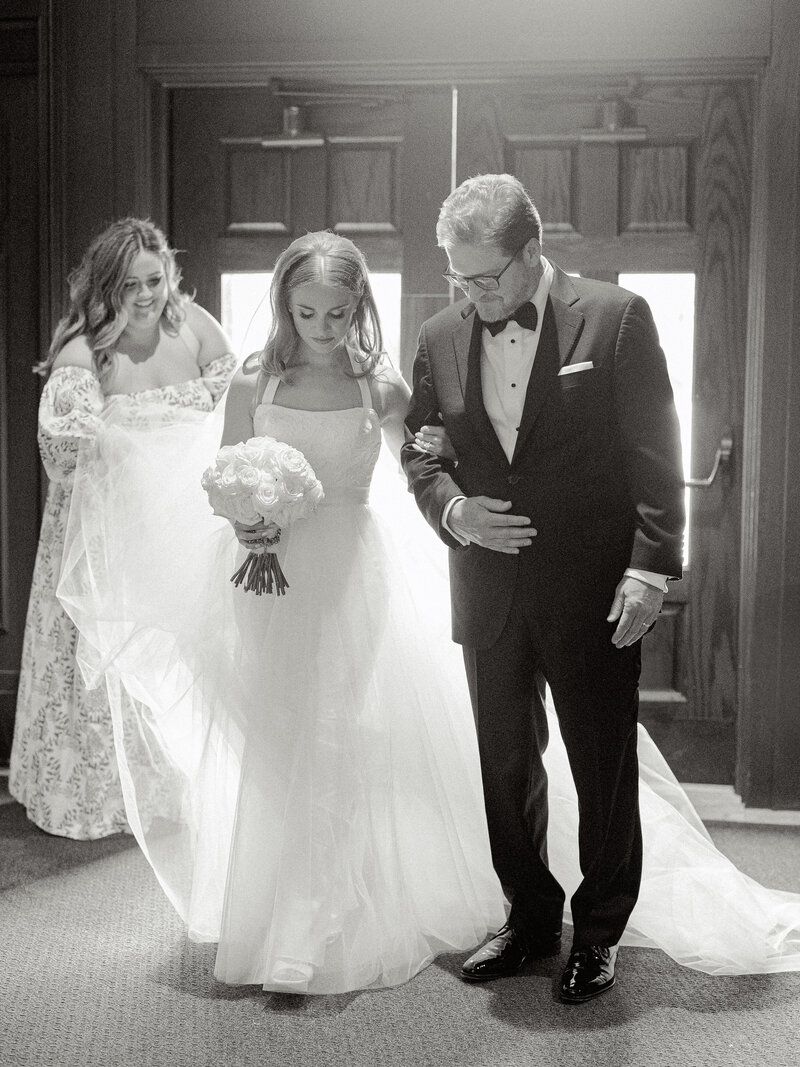 Black and white photo of a bride and her father sharing a moment before walking down the aisle.