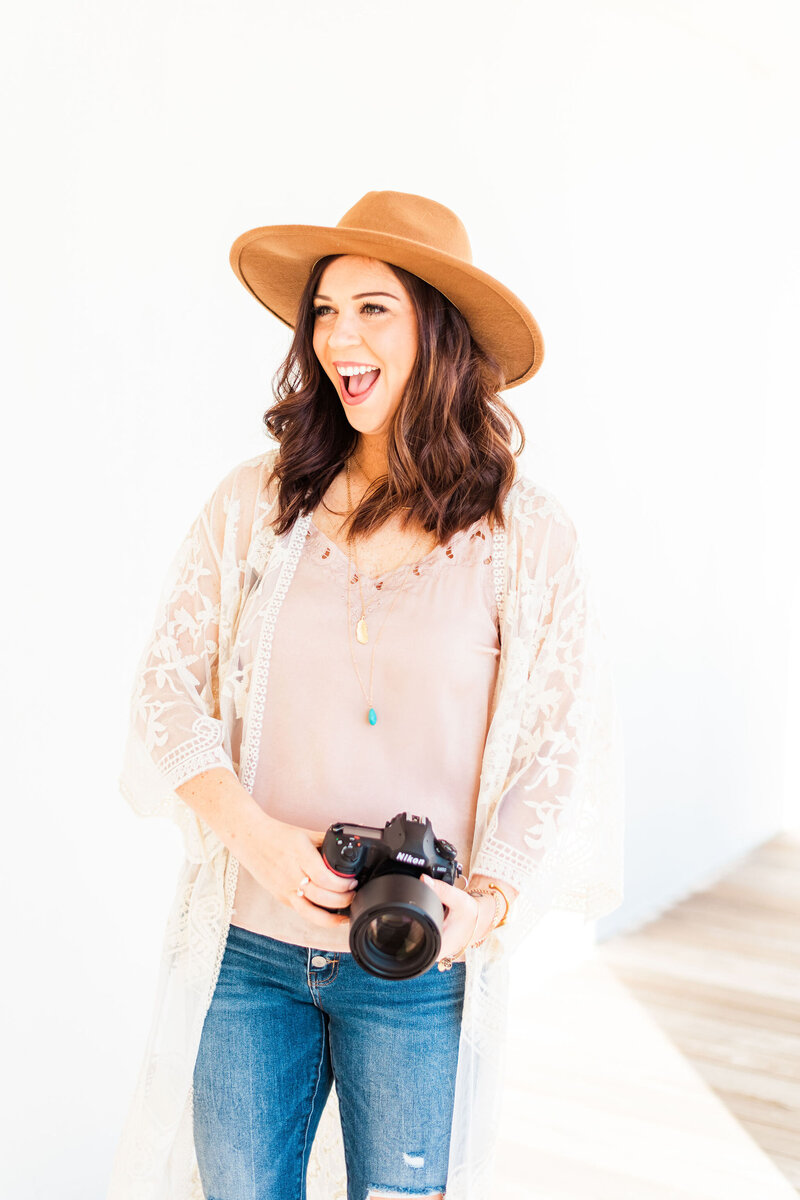 arkansas wedding photographer in a camel hat and pink tip holding her camera and laughing