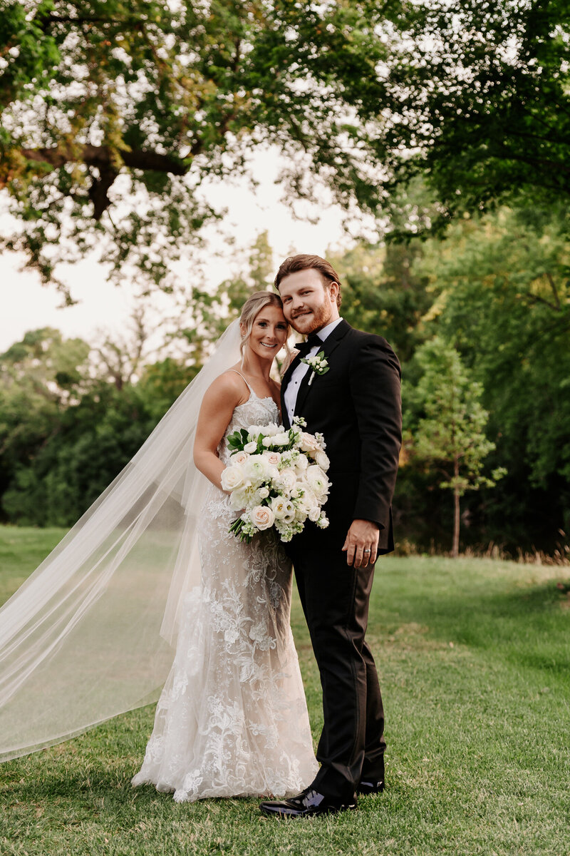 Newlyweds standing together smiling as one holds a bouquet of flowers