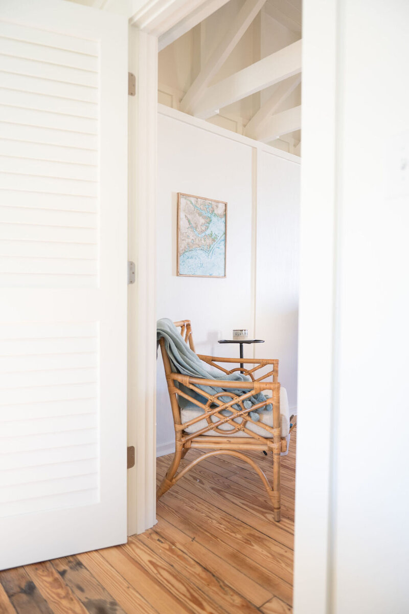 a boho rattan chair with a framed canvas of a watercolor painting featuring a coastal map with a candle on the round coffee table