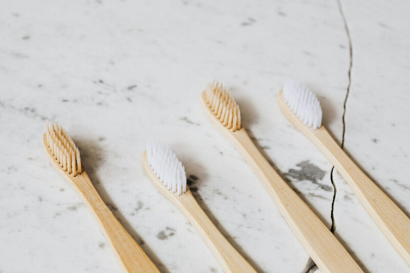 Four wooden toothbrushes used for dental exams and cleanings, laying on a white marble counter.