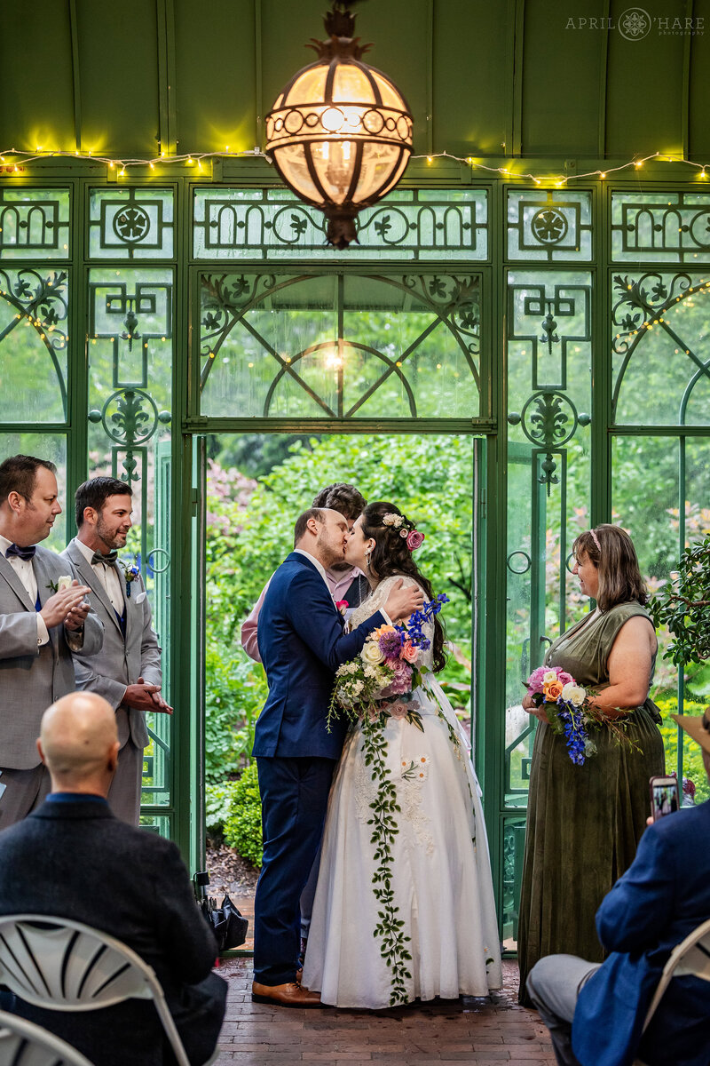 Groom kisses his bride at their wedding ceremony at Green Solarium at Denver Botanic Gardens
