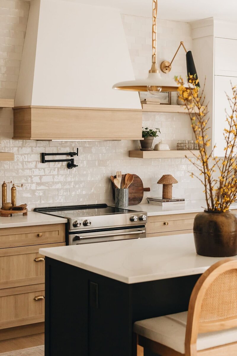 Custom kitchen hood with light wood trim, white zellige tile backsplash, and stainless steel stove in a modern Montreal kitchen – by Ingrid Interior Design.
