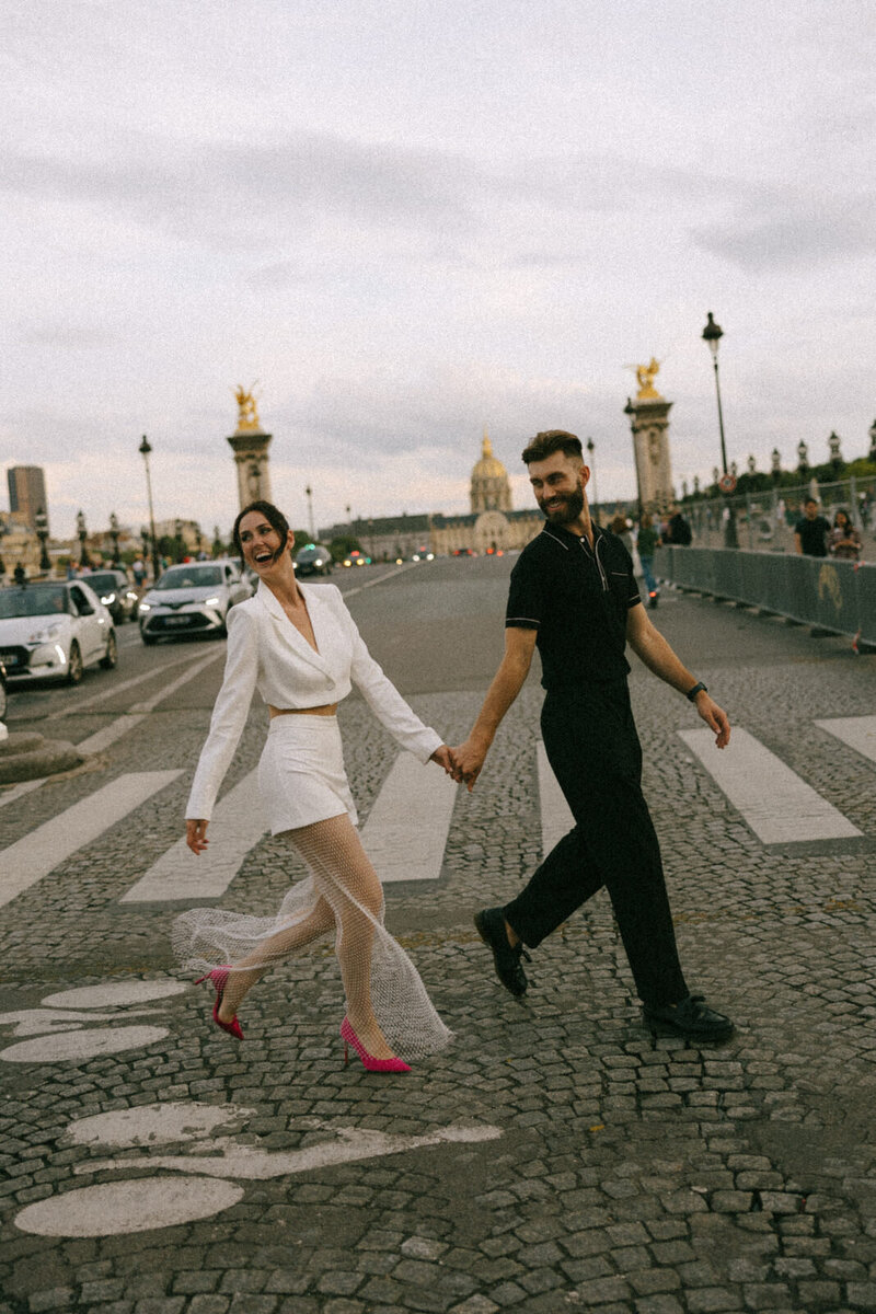 A man and woman walking across a cobblestone road in Paris France, captured by Andrea-Marie Photography