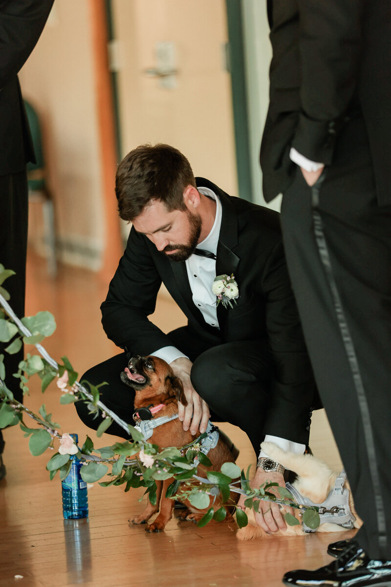 Groom bending down to pet his dog during the wedding, sharing a heartfelt and joyful moment of love and companionship.