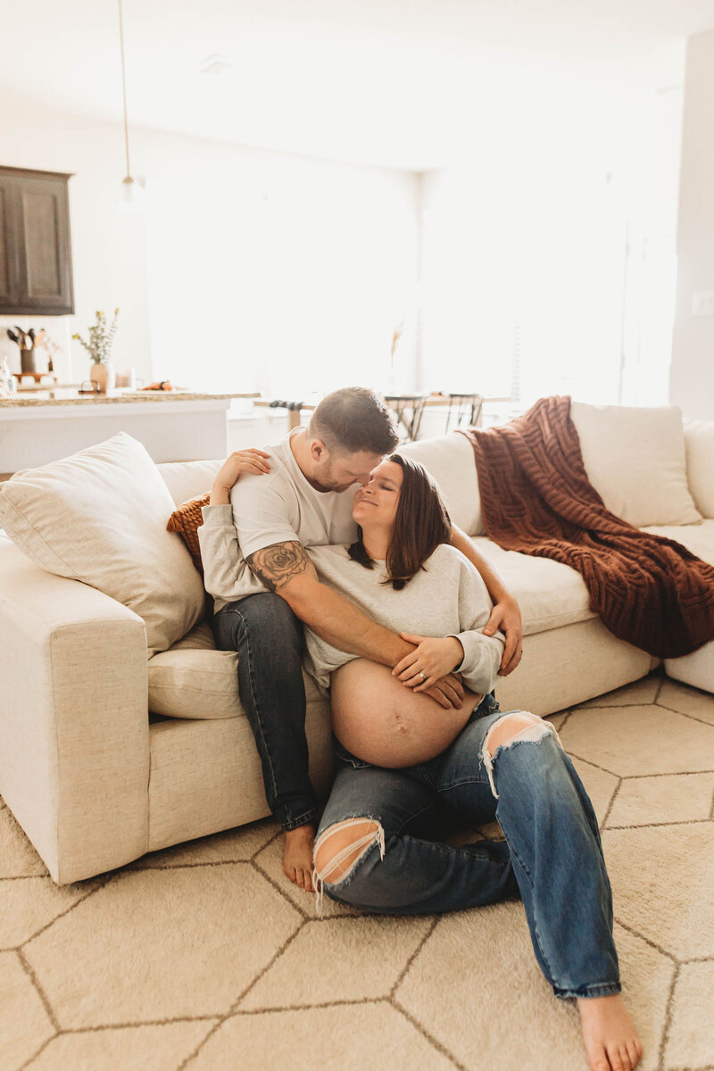 husband sitting on a sofa leaning down and holding his pregnant wife
