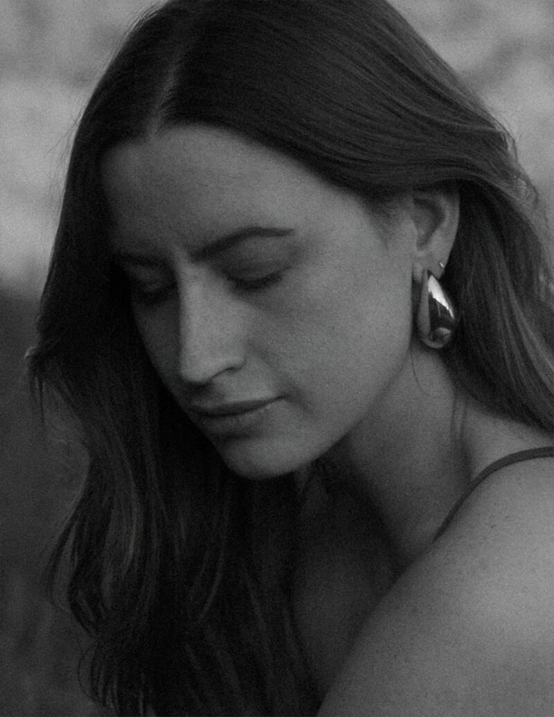 wedding photographer self portrait as the beautiful brunette woman is wearing an all white pant suit, gold rings and large pearl and gold vintage earrings.