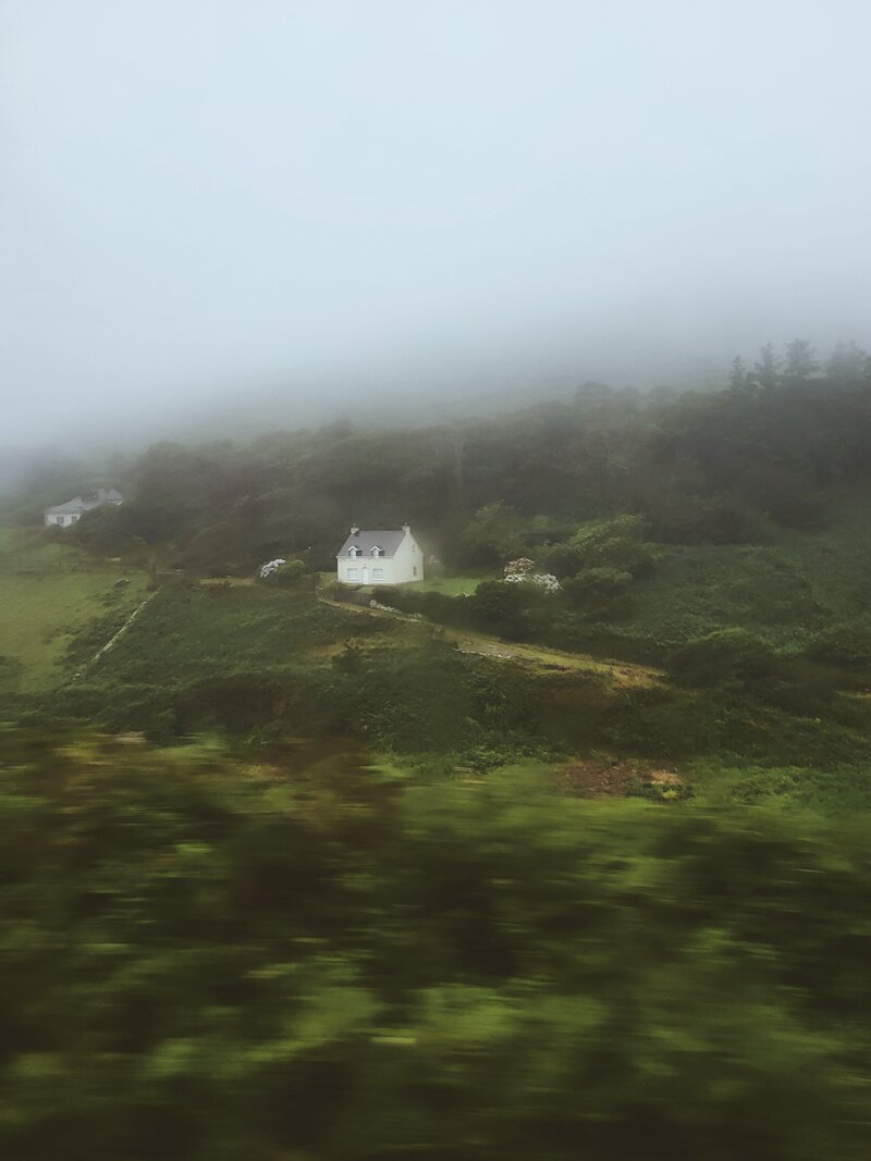 beautiful simple  white house with 2 gables on a hilside on a very cloudy day in Ireland