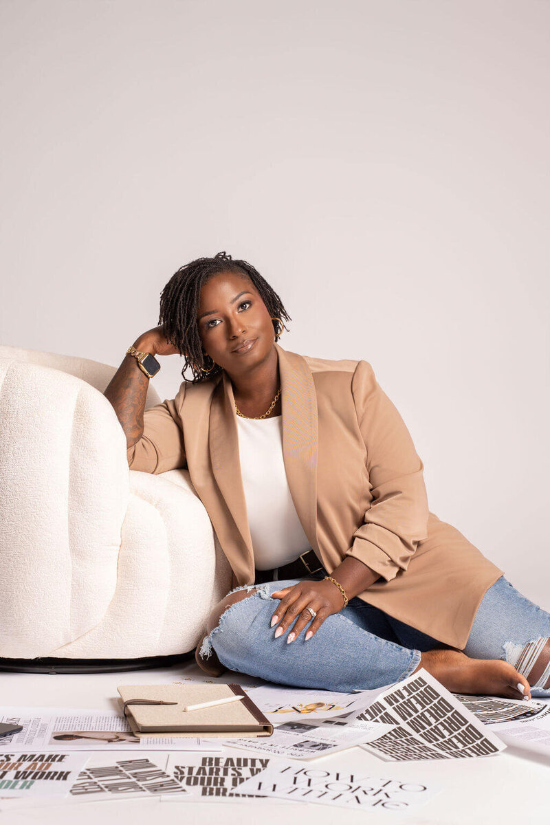 Female web designer for real estate and builders seated confidently next to a modern accent chair.