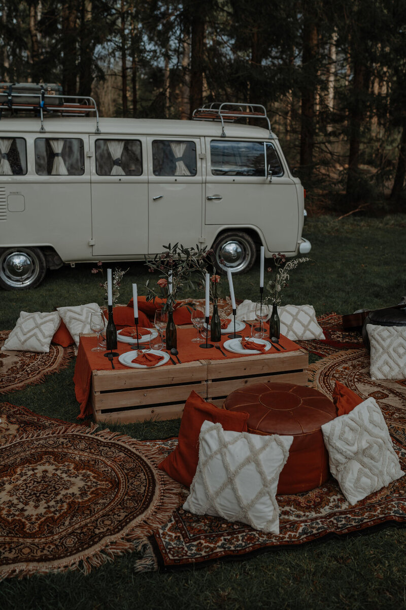 Diner setting voor bruiloft in camping met kussentjes, bohemian tapijten en vw vintage trouwaouto