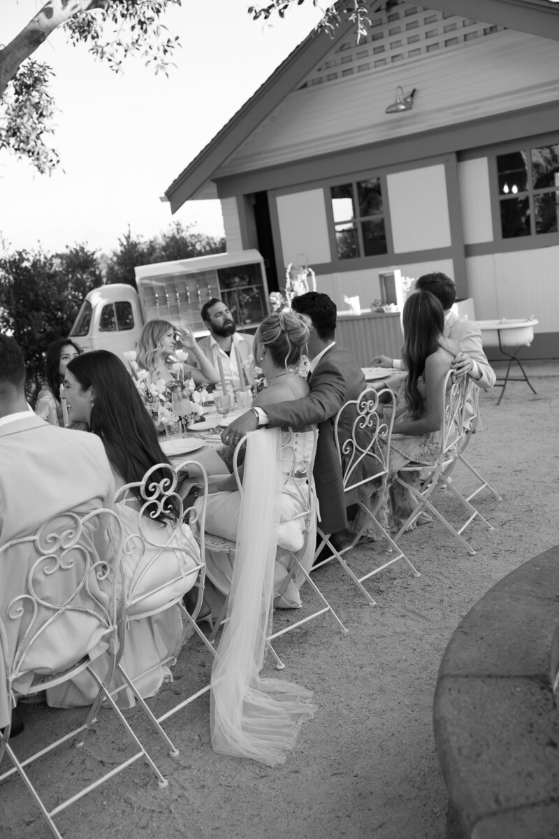 Bride and groom at their reception table surrounded by the wedding party, enjoying laughter and celebration at their California wedding in La Jolla.