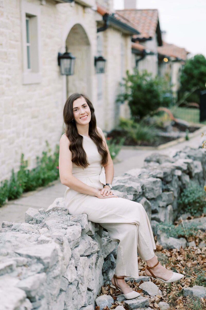Aurore bridges a wedding photographer in dallas sitting on a stone wall with her hands crossed looking and smiling at the camera