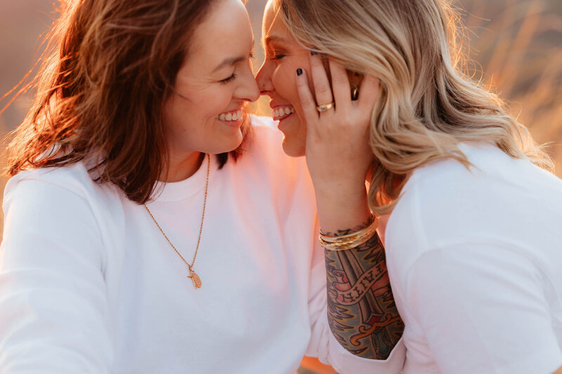 A same-sex  couple smiles and leans in for a kiss  at their engagement session