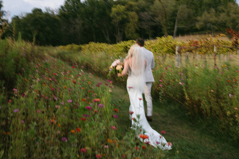Warm, motion-blur image of bride and groom walking through flower field at Nashville wedding