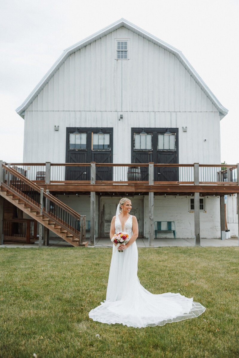 Bride poses for portrait in front of white barn wedding venue at Lincoln Farmstead