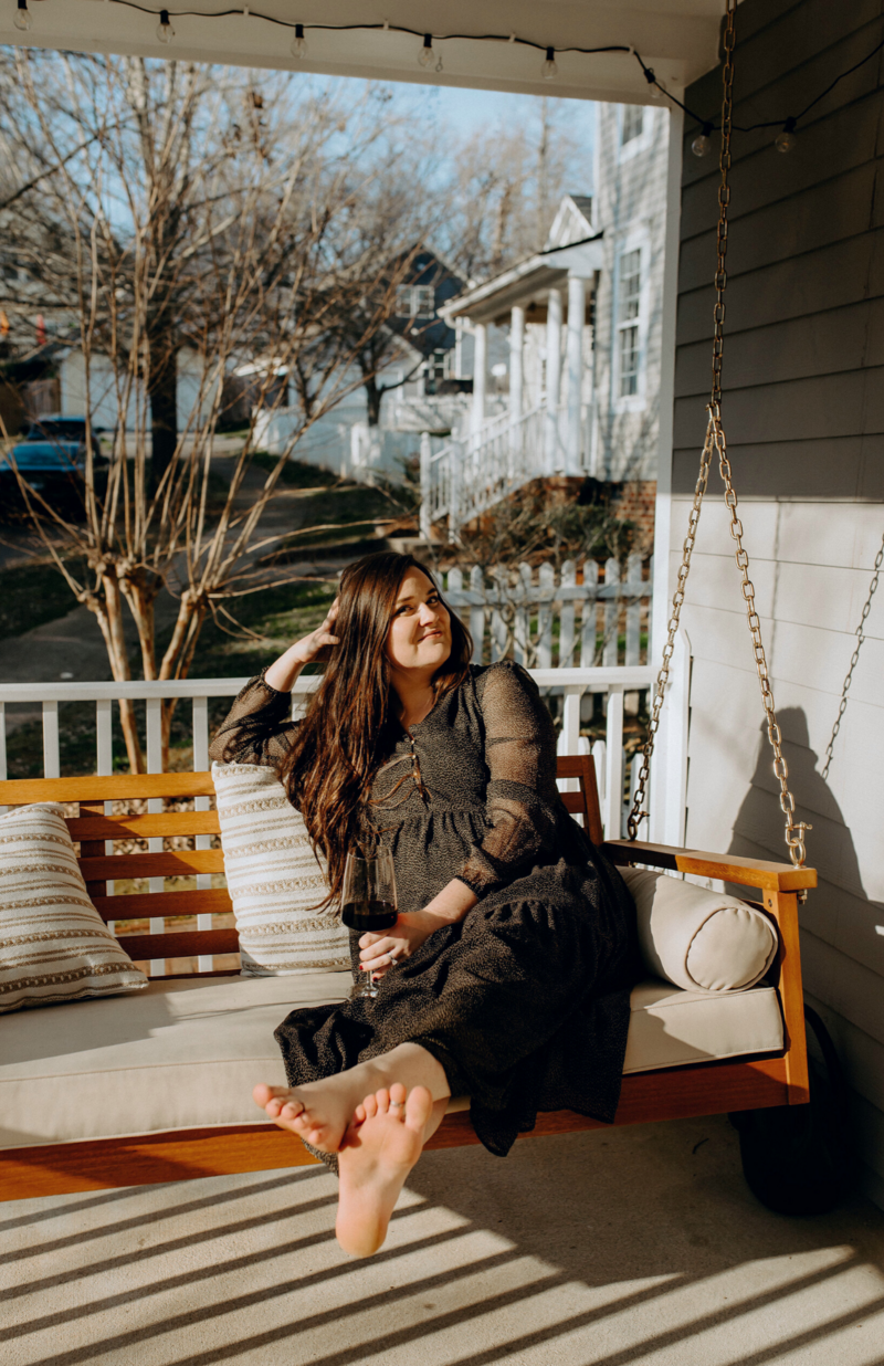 Copywriter, Abigail Rudnitsky, sitting on a porch swing, smiling and holding a glass of wine