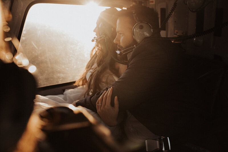A bride and groom embracing in a helicopter, bathed in golden sunlight.