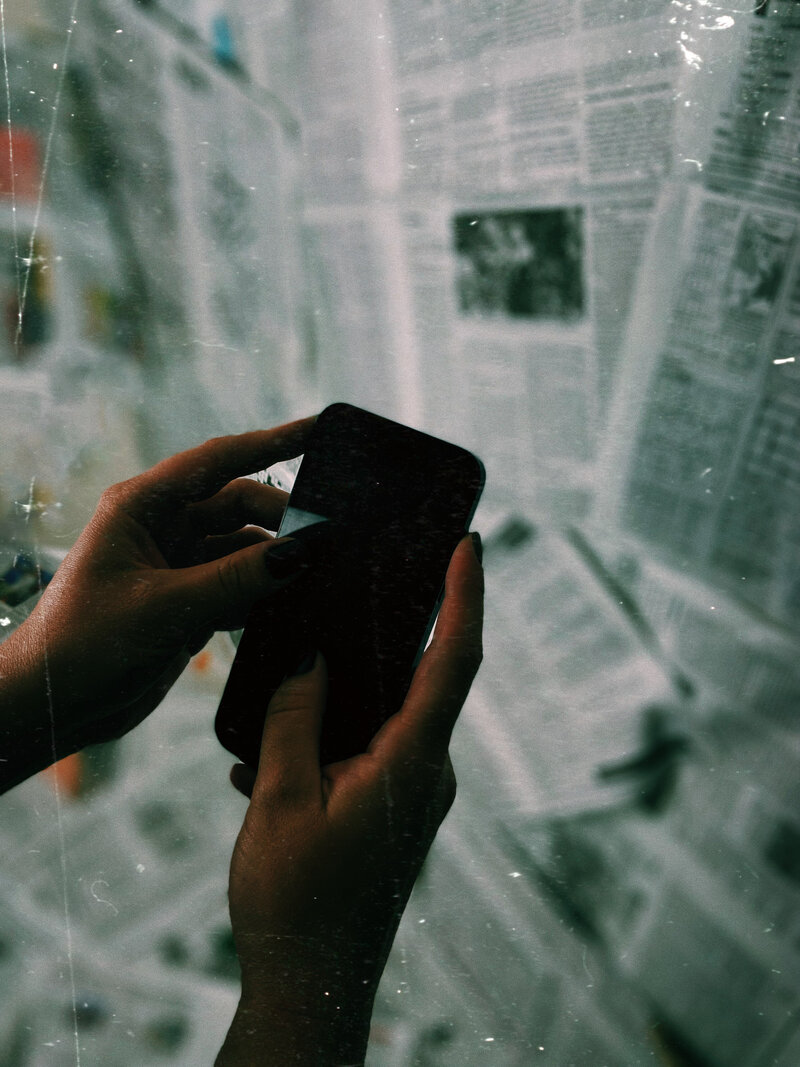Photo showing hands holding a smart phone with blurry newspaper background