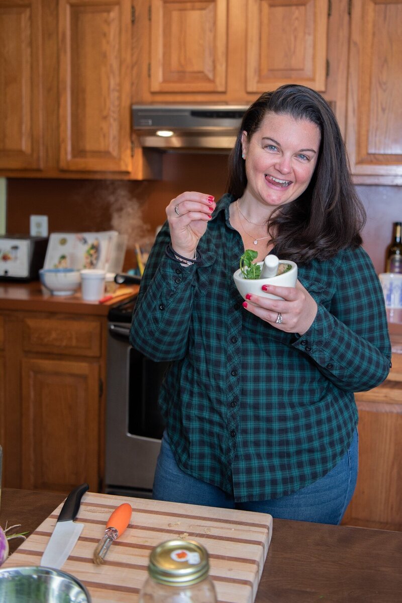 A woman smiling in her kitchen holding a mortar and pestle.