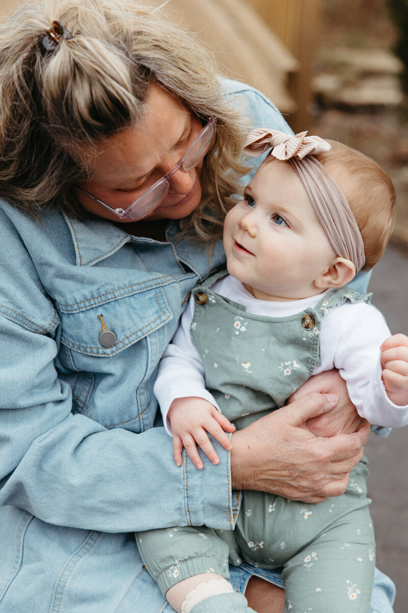 Grandmother holding baby grand daughter while they smile at each other taken during an extended family portrait session. 
