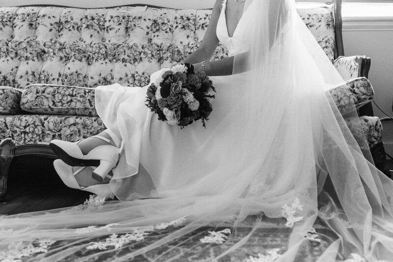 Bride sits on settee holding her wedding bouquet