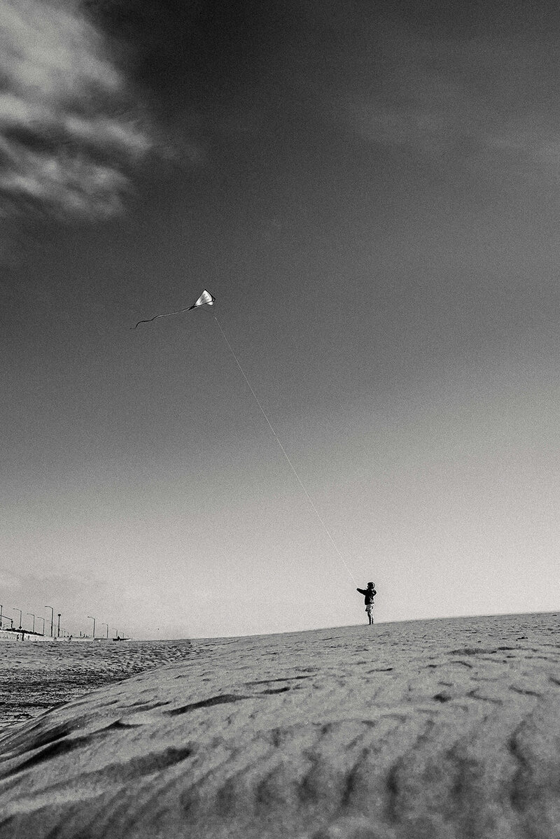 Black and white environmental portrait of girl and kite on San Francisco beach
