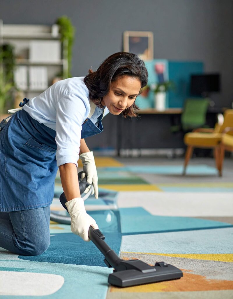 professional cleaning woman, vacuuming the carpet in a trendy commercial office space