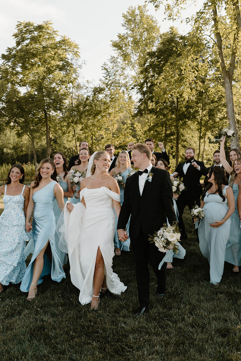Married couple walking down a grassy hill with their bridal party, celebrating together after the ceremony in Columbus, Ohio.