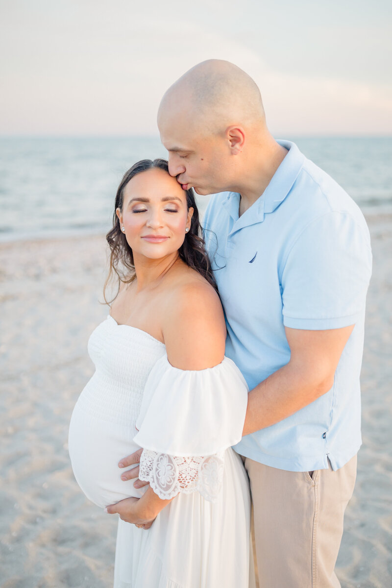 A tender moment captured by a Connecticut maternity photographer—a husband gently kisses his wife's head as she closes her eyes, dreaming of the day their baby enters the world, love and anticipation filling the air