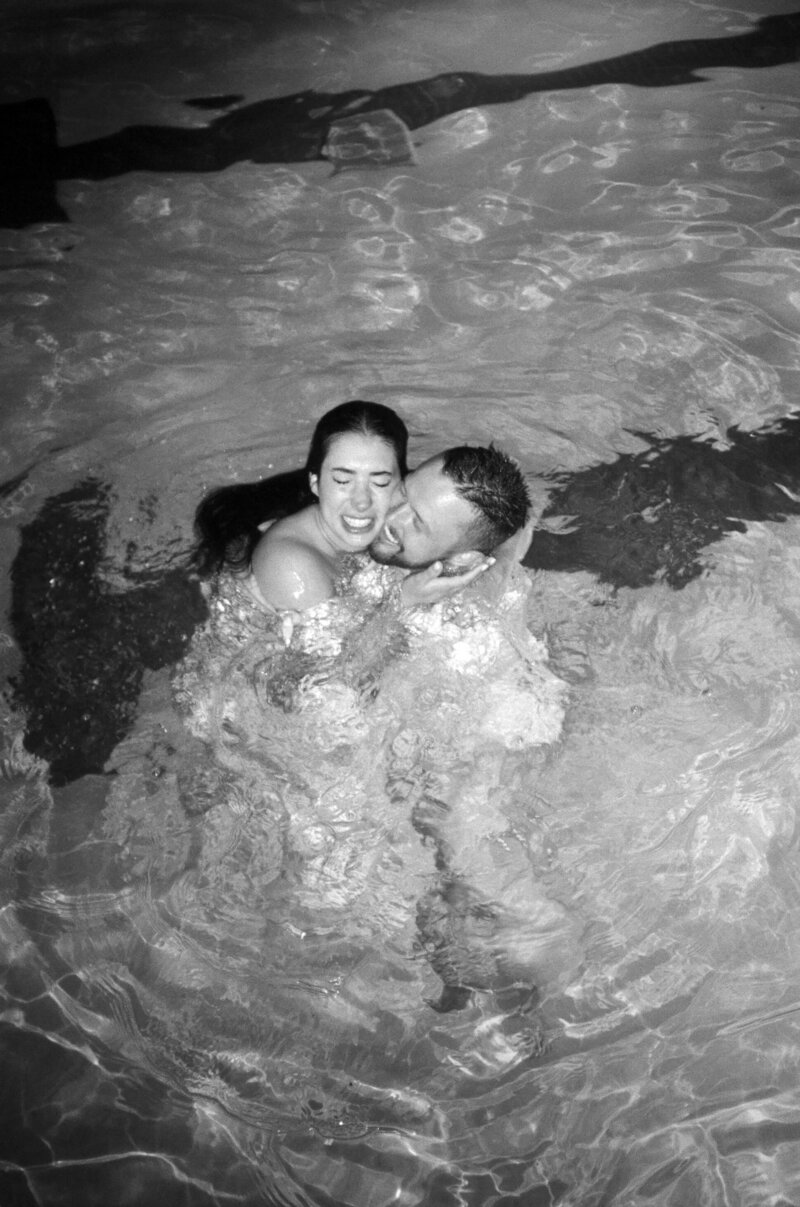 Black and white film photo of bride and groom in the pool in their clothes at Brasada Ranch.