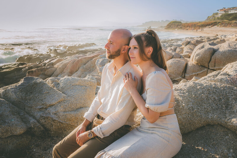 A bride holds onto her groom's arm as they sit and enjoy the ocean in Big Sur.